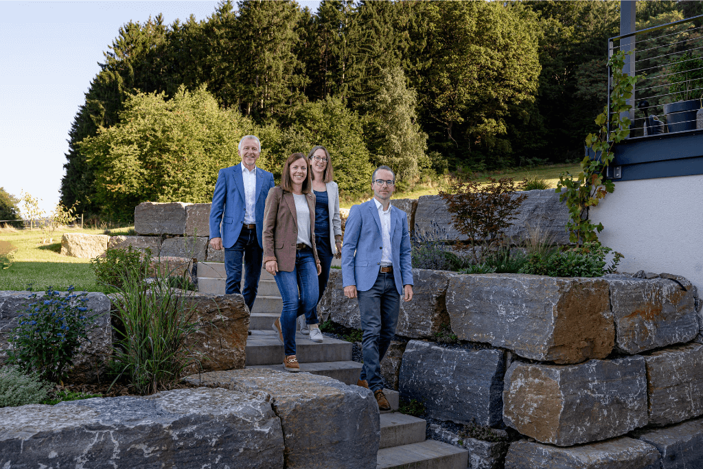 Immobilienmakler im Odenwald. Die vier Köpfe von Mühlfeld Immobilien gehen eine Steintreppe im schönen Wahlen hinunter.
